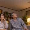 夜のリビングで天井裏の物音に不安そうに見上げる夫婦