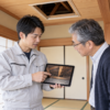 駆除作業員がタブレットで屋根裏の写真を見せ、60代の男性に調査結果を説明する様子